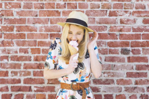 Girl with fedora hat bites into an ice cream cone in the summer and feels pain due to tooth sensitivity