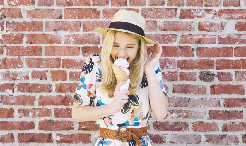 Girl with fedora hat bites into an ice cream cone in the summer and feels pain due to tooth sensitivity
