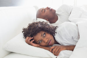A woman lays awake next to her loudly snoring husband, hoping he’ll take advantage of dental solutions for sleep apnea soon.