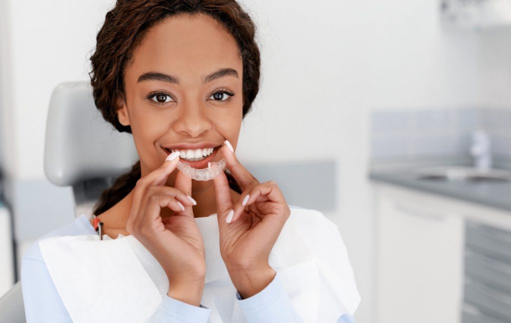 A young Black woman holds her aligner tray after deciding between Invisalign vs. Smile Direct.