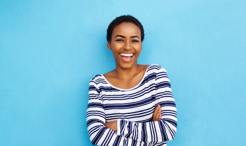 Portrait of happy young black woman laughing against blue wall