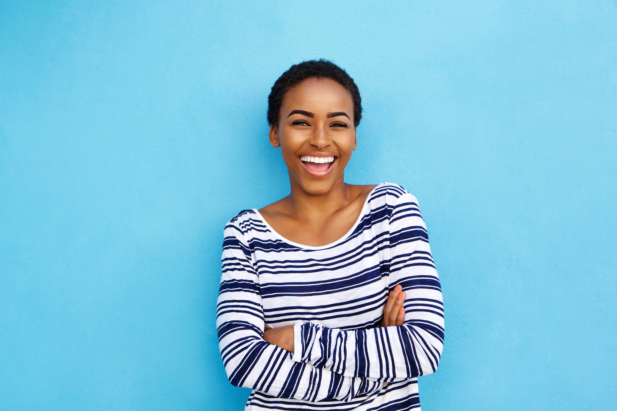 Portrait of happy young black woman laughing against blue wall